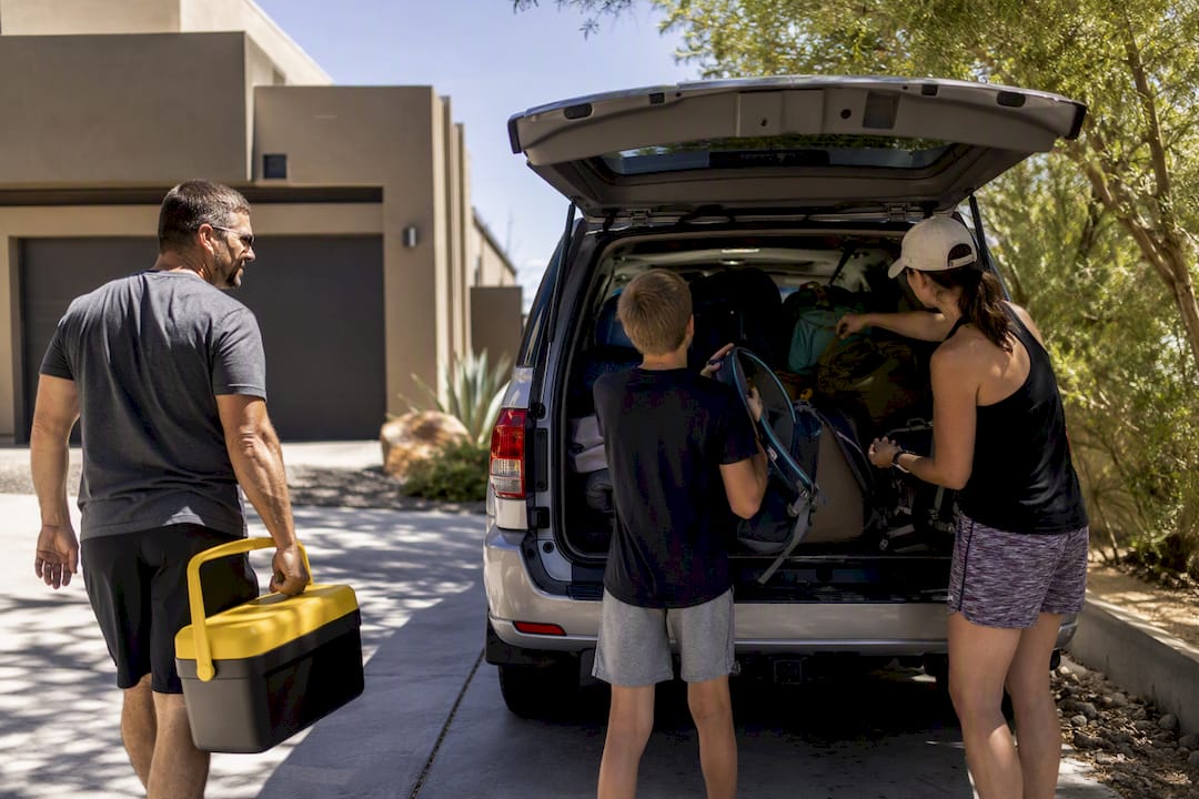 Family packing hiking gear into car trunk